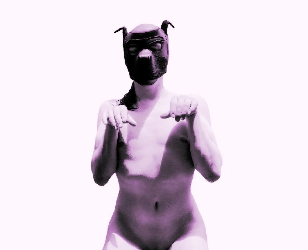 A purple tinted monochrome picture of me kneeling with my hands up like a dog. Wearing nothing but a pup hood. The picture is cropped just above the genitals
