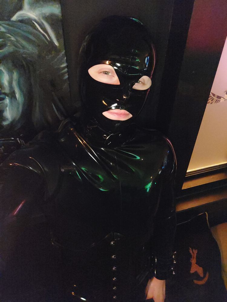 The gimp is at another bar. This picture was from the final night of MRW. The gimp wears a rubber catsuit, hood, and corset.