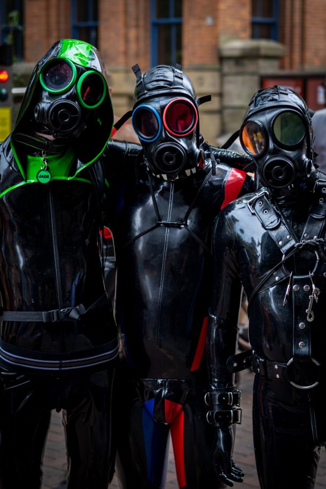 Three rubber drones stand in a line.
The left drone with green accents is @jadedrone.
The middle drone with blue and red accents is @xantw0.
The right drone in all black with restraints is @rubberjohan.
This fantastic photo was taken by @riot.photos
