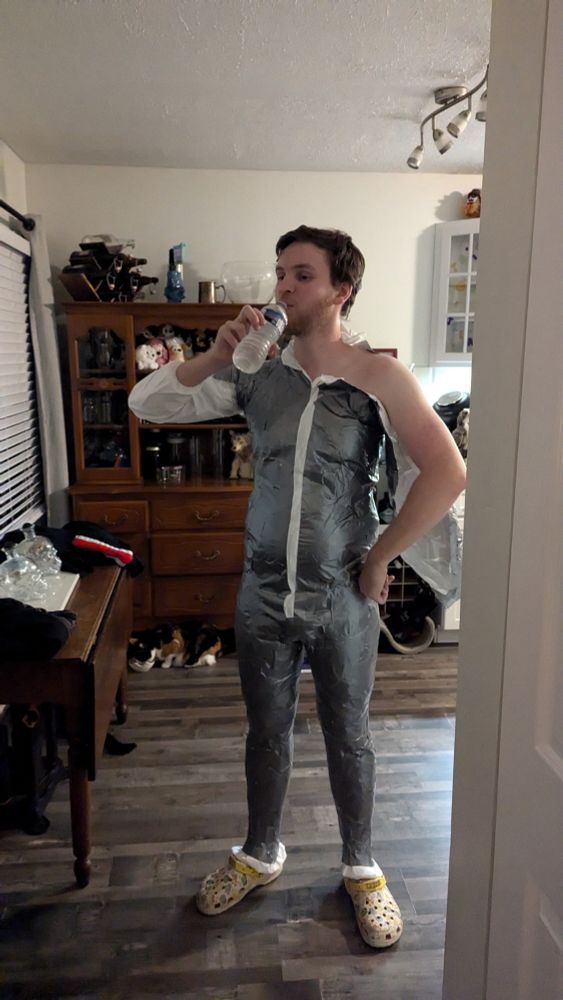 My husband, taking a short break from being tapped up, his left arm finally free - taking a drink from a bottle of water. He's wearing my pokemon crocks.