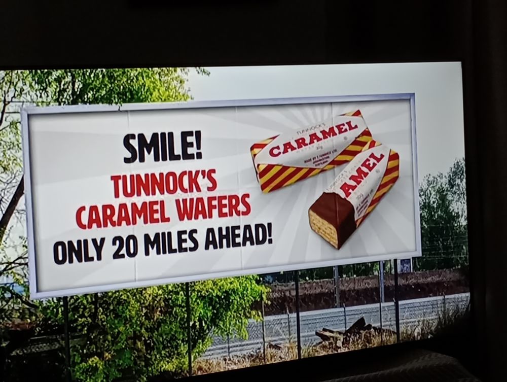New advert for Tunnock's Caramel Wafers as shown on ITV Friday 6 June 2025. The image shows a billboard advertising Tunnock's wafers with caption: "Smile! Tunnock's Caramel Wafers only 20 Miles Ahead!" 