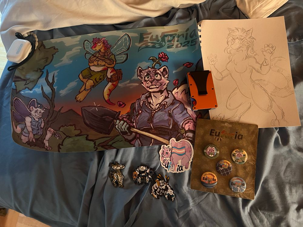 A collection of all the goodies purchased from the Dealer’s Den, such as the 2025 Solarpunk poster, a trans pride vinyl sticker, and a set of 5 buttons, all bought from Eufuria’s own booth. On the right is a sketch of my own character, Ollie, commissioned from BushyCat during the first vendor hall.