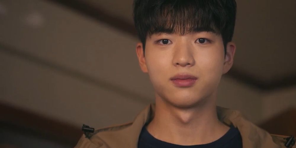 Actor Cha Kangyoon as Jiho, one of the main characters in "Head Over Heels" looking into the camera, wearing a beige jacket. He has a tiny smile on his face and tears in his eyes.