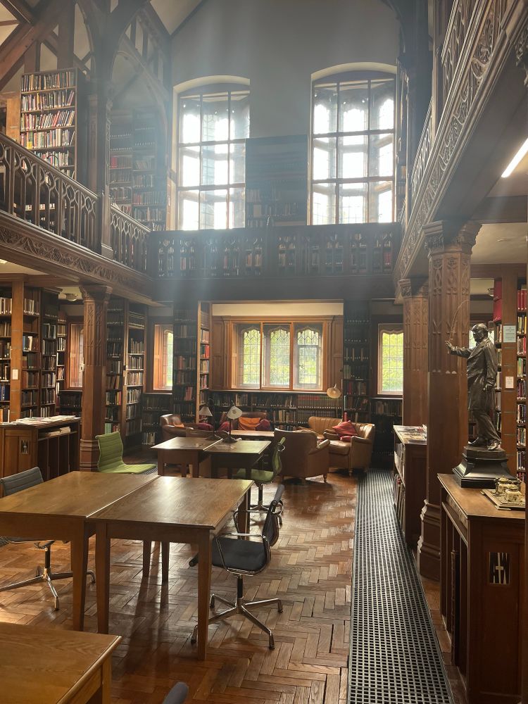 An Edwardian library reading room, with shelving, wooden desks, armchairs and a wooden gallery above.
