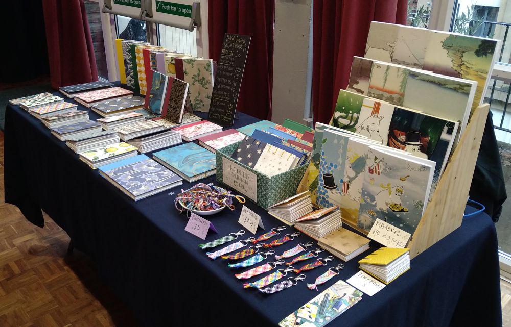 A photograph of a table at a craft fair, laid out with many handmade sketchbooks.
