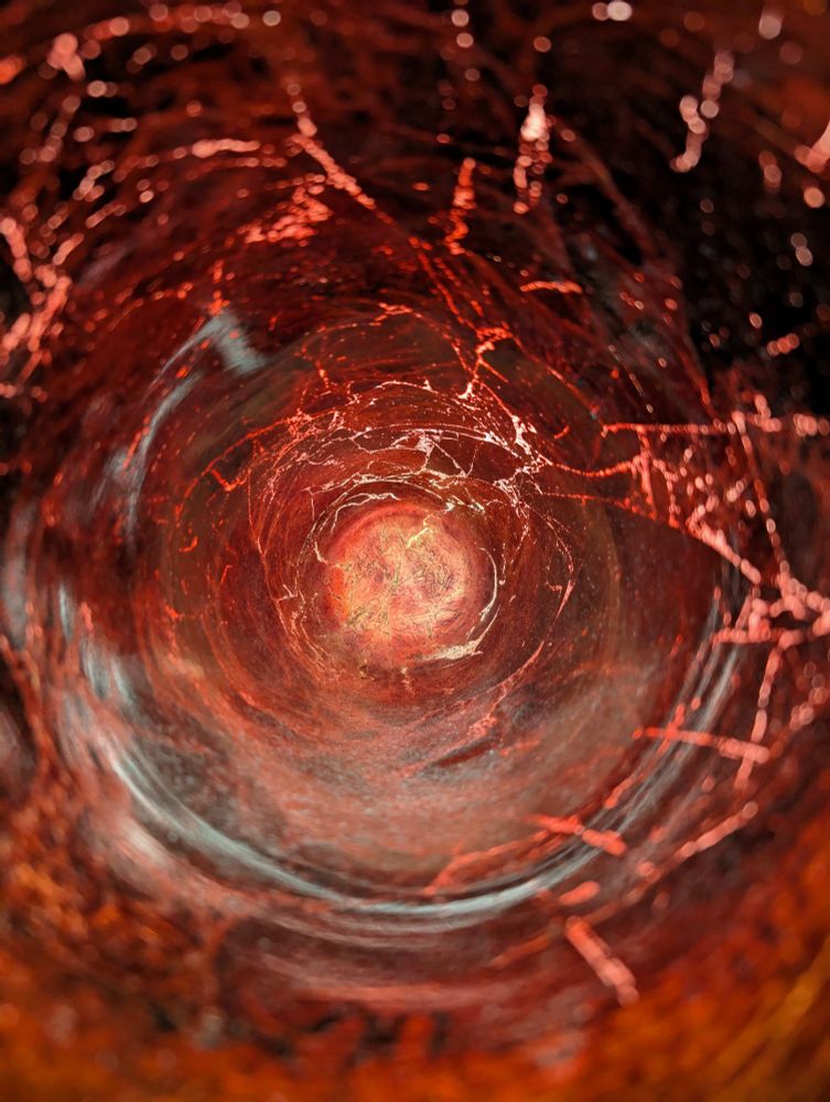 Similar photo to the first one. The inside of a copper colored vase. The camera is positioned on the inside such that you only see the center, hiding the fact that it's a vase. The light shining on the outside illuminates the inside, making it seem like a funnel shaped storm.