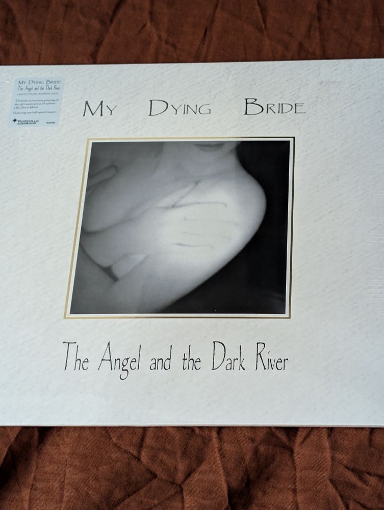 The front of the album "The Angel and the Dark River" by the British Doom metal band My Dying Bride. Originally released in 1995 as the band's third studio album, this is a 30th anniversary special re-release.

The album cover is white. At the top is the band's name (My Dying Bride) while at the bottom is the album title (The Angel and the Dark River).

In the middle is a photo of a woman's unclothed torso. Her bare arms are crossed to cover her chest with her head turned to the side. The photo goes up to her lips, so you don't see the rest of her face. The background of the photo is black.