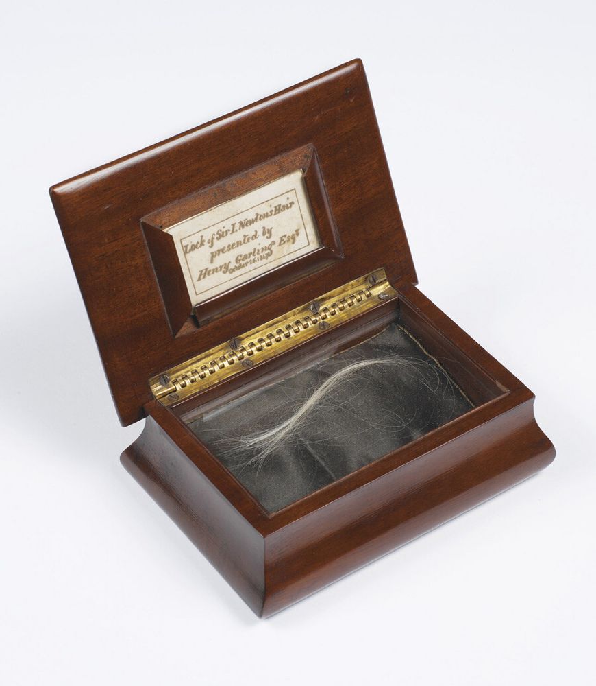 A mahogany box with the lid open. Inside are several stands of light colored hair. The box has an plaque that reads: "Lock of Sir I. Newton's Hair presented by Henry Garling Esq. Oct 26 1847."