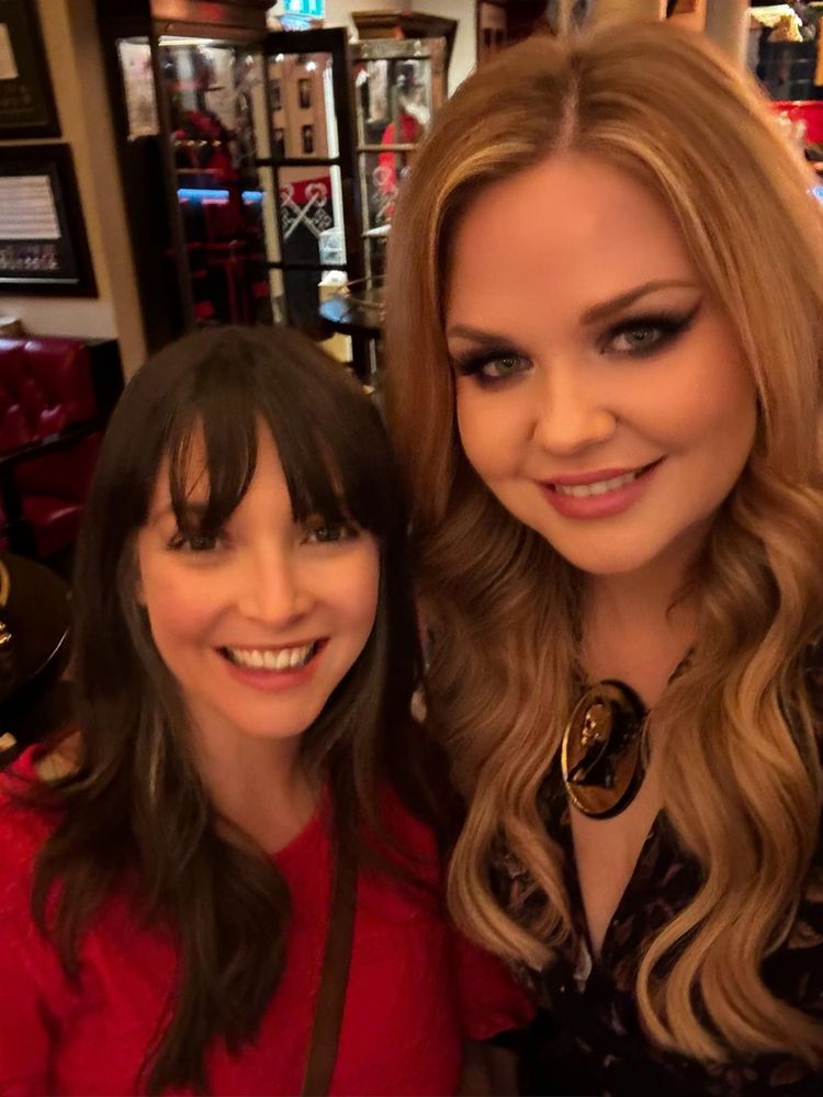 A photo of Chloe in a read dress and Lindsey with long blonde hair smiling at the camera. 