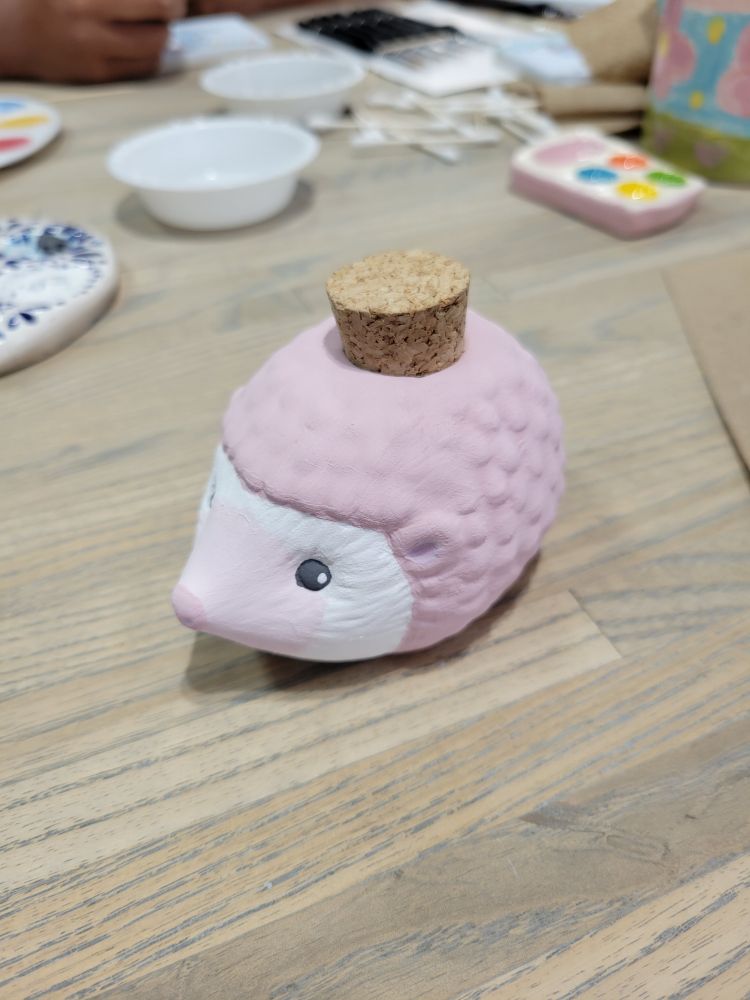 A ceramic hedgehog jar sits on a table. The hedgehog is painted pink. 