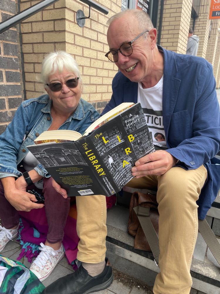 David and friend Sheila looking at a book, The Library: A Fragile History, on the steps of the new library, which has yet to open. Belbin is wearing a 'Plasticine Action' T-shirt and got enquiries about where to buy one.