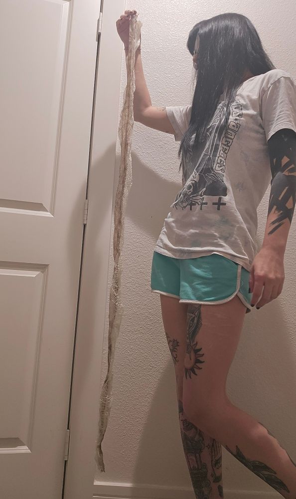 A person with long dark hair holding up a the shed skin of snake