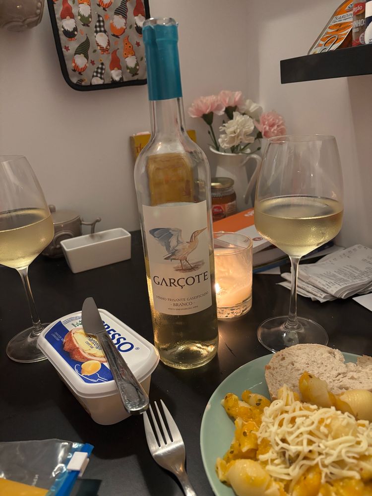 A simple meal with wine and bread on black table top.  there is a lit candle in a glass and a small tub of butter labeled "gresso" in Portuguese. 