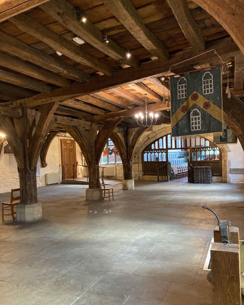 We are looking at a large room known as the Undercroft which has central wooden posts that branch out to hold a wooden ceiling (which is also the floor of the Great Hall above). The floor is stone flagged. 