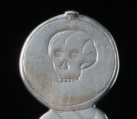 We are looking at a close up of a silver spoon showing a tiny engraved skull. Which if a skull can be is quite cute. 