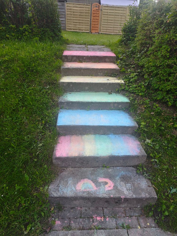 Eine Treppe, die mit Straßenkreide in Regenbogenfarben angemalt ist, unten ein zwei Regenbögen 