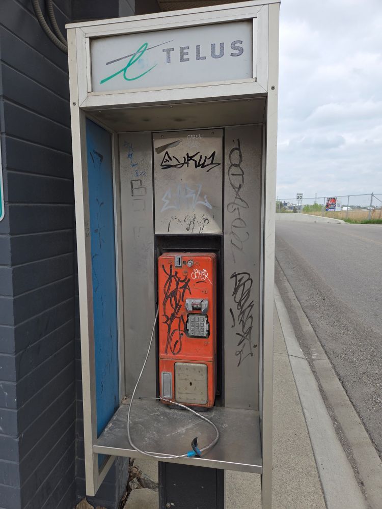 An abandoned and vandalized phone telus phone booth.