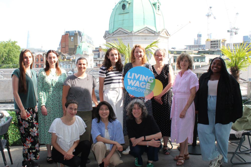 The Bridge Group team grouped in front of a London skyline, holding a 'Living Wage Employer' sign.