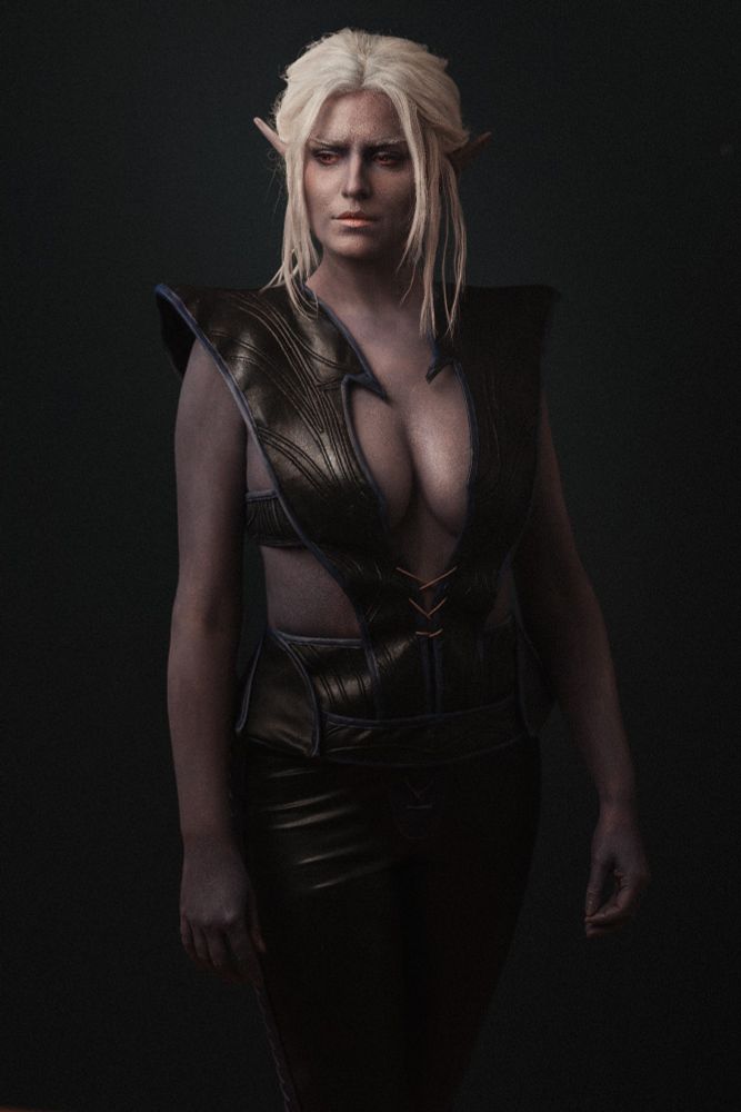 Minthara, A Drow standing in Front of a black wall in her Camp Outfit