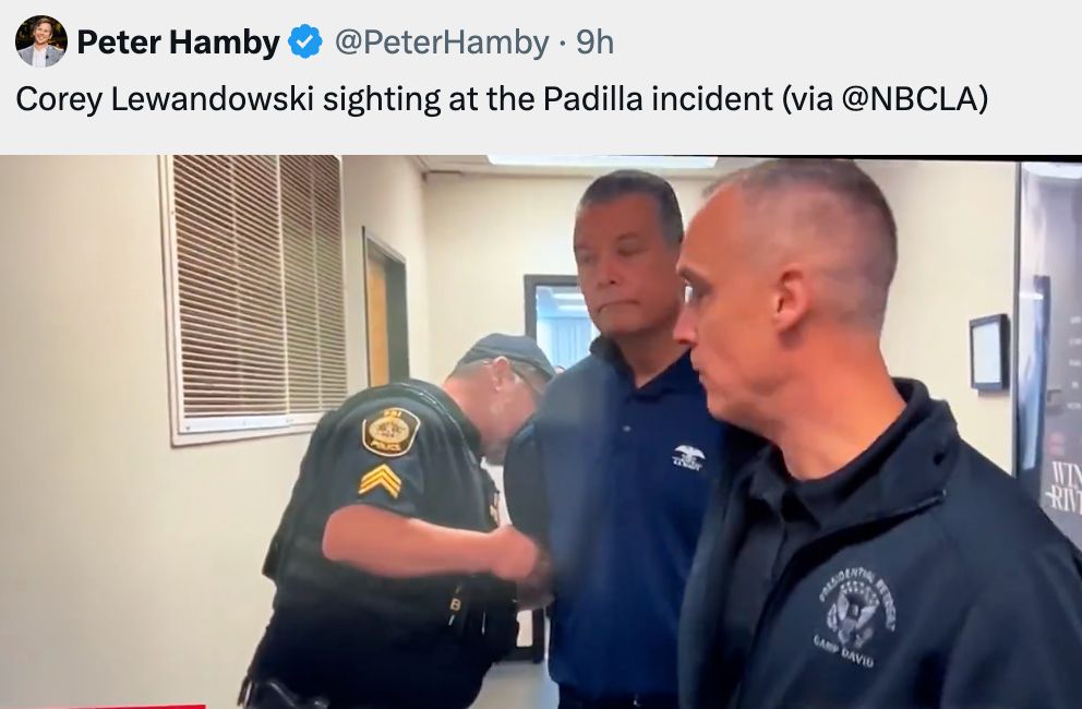 A screencap from a video posted by Peter Hamby. It shows that a cop taking the cuffs on Senator Padilla, with Lewandowski, wearing a black jacket with what might be a Homeland Security logo, watching.