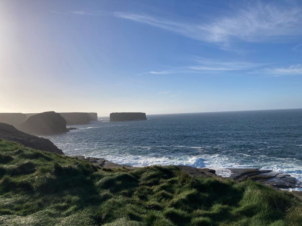 Cliffs outside of Kilkee, County Clare. The waves are crashing onto the rocks below. The sky is crystal clear.
