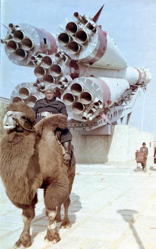 A man mounted on Bactrian camel's back poses for a photo in-front of Soyuz rocket, (1980s), Baikonur, Kazakh SSR. Photographer unknown