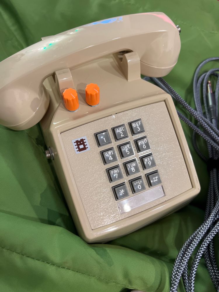 Photo of a telephone with two orange dials above the number pad sitting beside a guitar cord.