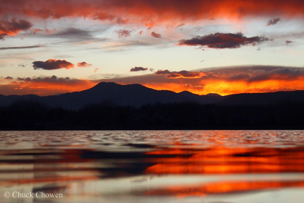 Orange sunset clouds above a mountain. A red cloud above reflected in the water below