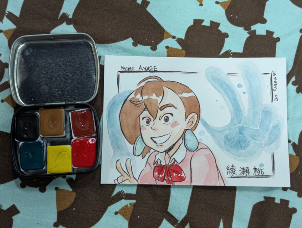 A mini watercolor pallet with 6 paints next to a 3"x5" colored drawing of Momo Ayase and her spirit hand.