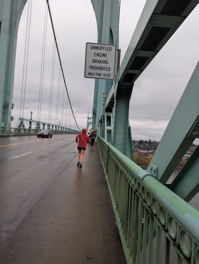 A rainy day shot of the deck of the St. John's bridge. Some runners are running on its sidewalk farther ahead.