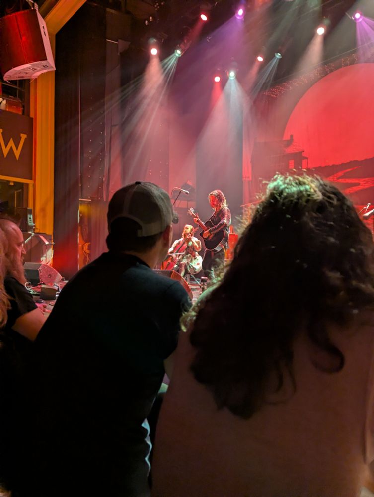 Pic from the show. A guitarist and cellist together on stage, framed between two audience members.