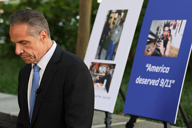 Andrew cuomo standing in front of a sign that says “America deserved 9/11”