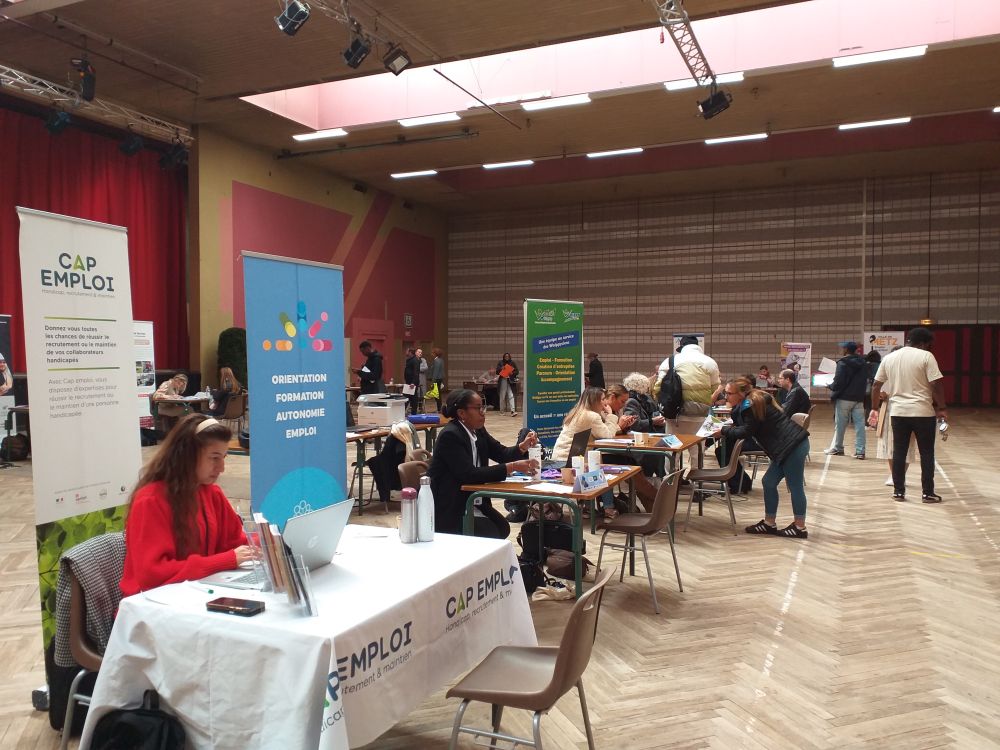 Vue sur l'ensemble du salon avec plusieurs stand et celui de Cap emploi 57 au premier plan. Une action organisée par la MEF de WOIPPY, en collaboration la ville de Woippy, France Travail, Cap emploi, et la Mission locale.