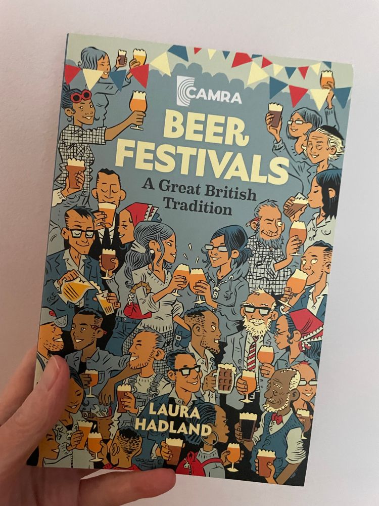 My hand holding a copy of Beer Festivals: a great British tradition by Laura Hadland. The cover consists of a colourful illustration depicting a diverse variety of people happily drinking beer.