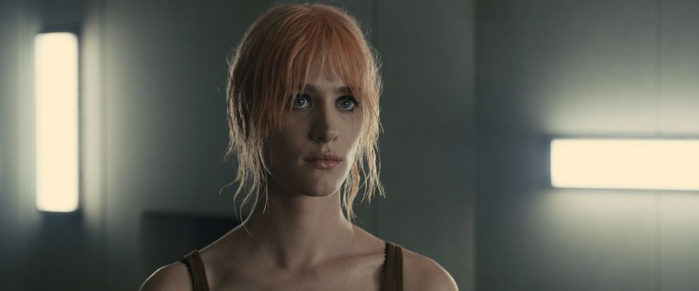 A photo of Mackenzie Davis in the film Bladerunner 2049. Her character has shaggy faded pink hair.