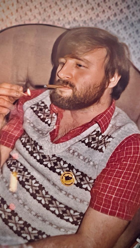 A bearded man smoking a cigar from approx early 1980s. 