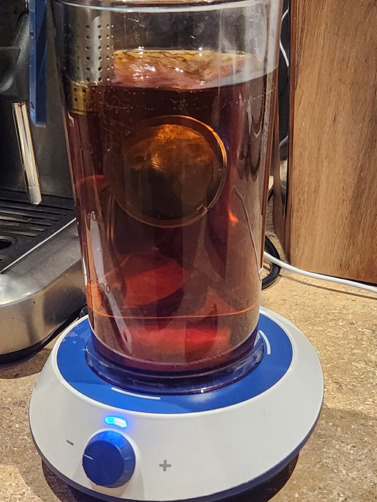 A container of cold brew tea with infusers and stirrer bar inside, atop a magnetic stirrer.