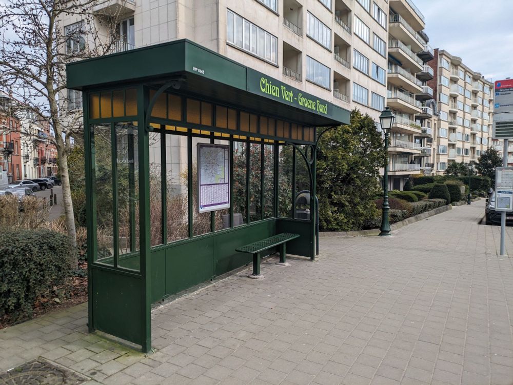 A dark green tram stop with yellow glass in lead and decorative swirls in the front 