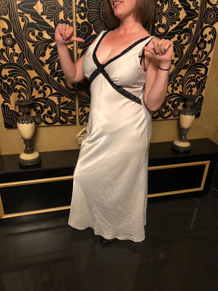 Blaise wearing a long white gown, gesturing to herself with both thumbs