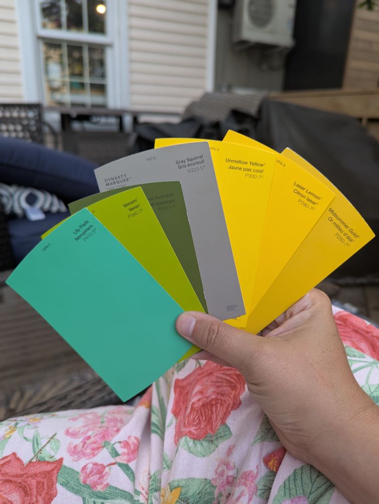 An array of paint chips, with a teal, a green called "venom", a dark avocado green, a dark grey and three different shades of bright yellow