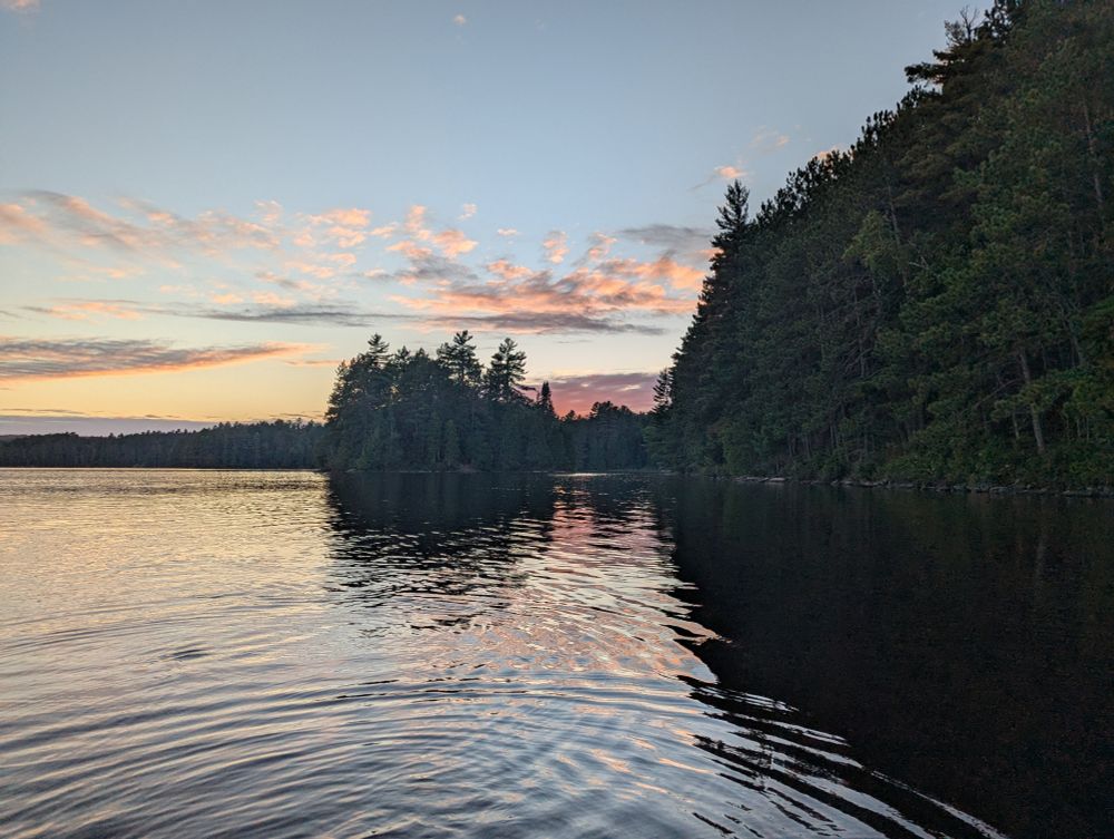A sun set against a pine forest reflected on the lake