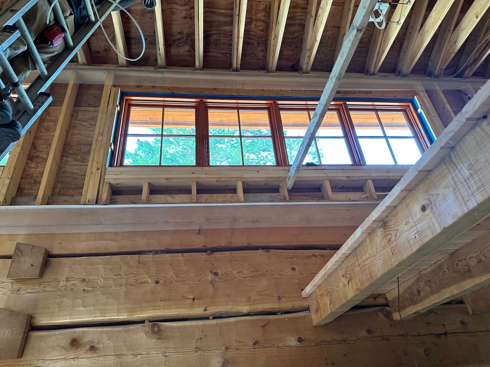 Stained & Clear coated Fir window installed high overhead in an open floor area of a log cabin.