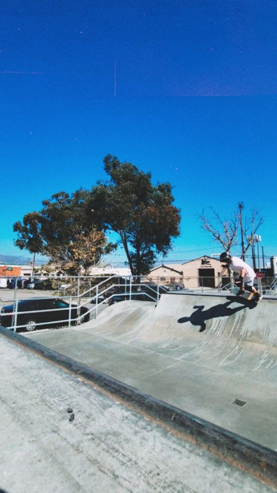 Ore is on the other side of the halfpipe mid grind.  We see their whole body now with a helmet on and wrist guards.