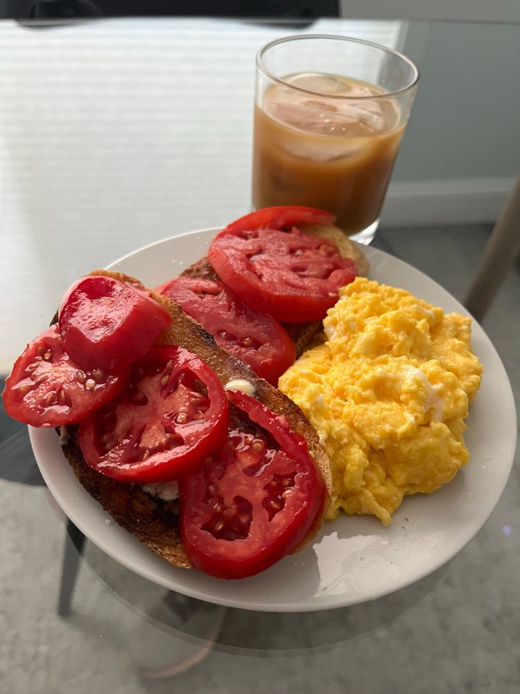 Two slices of toast with butter and tomatoes and a side of scrambled eggs 
