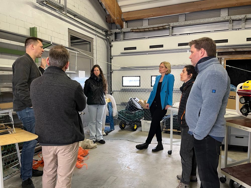 A group of people stand in the workshop and listen to an explanation. They are surrounded by technical stuff.