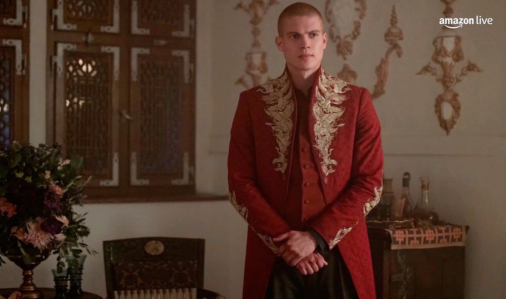 Rand al'Thor from the Wheel of Time, played by Josha Stradowski, wearing a fancy red coat with gold embroidered herons up the chest and collar and also along the sleeves.