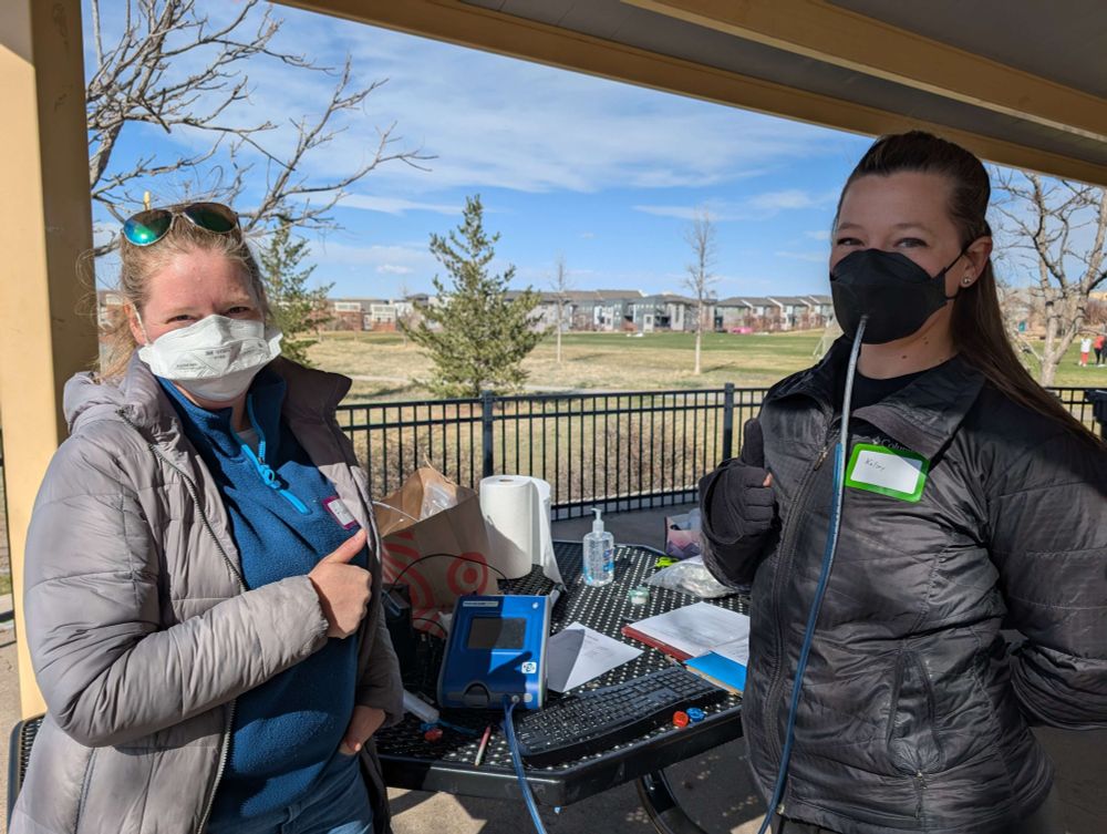 A participant being fit tested by Fiona with the PortaCount machine.  Both the tester and the participant are looking at the camera and giving a thumbs up.