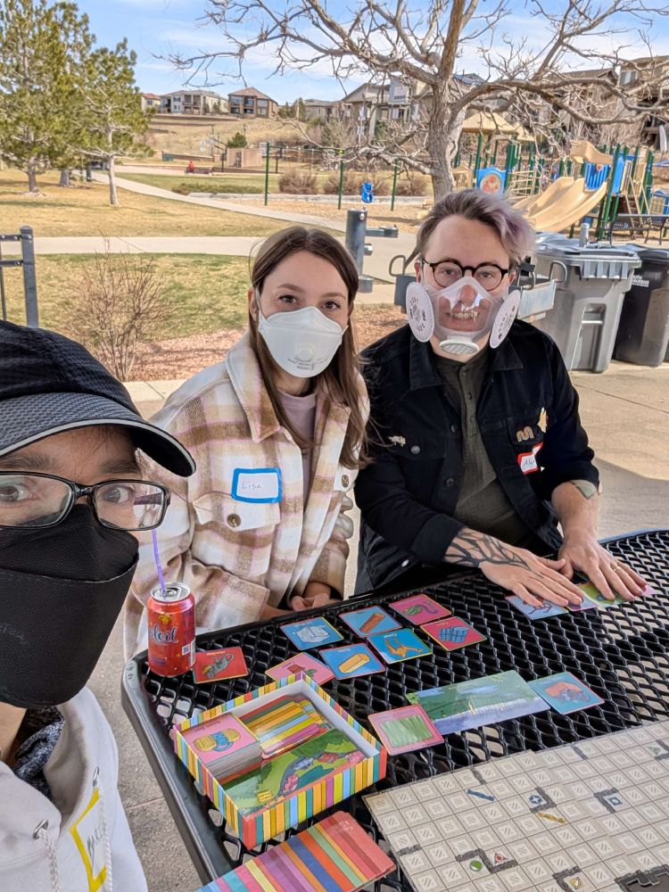 Three participants at the fit testing event playing a game in the waiting area on the picnic tables.
