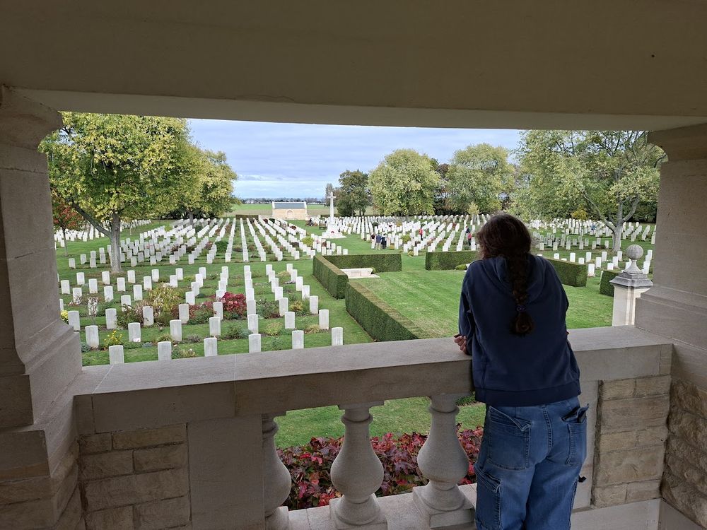 a pensive teen looking out over the Bény-sur-Mer Canadian War Cemetery, w/ many rows of graves in her line of sight.