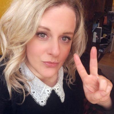 a photo of centrist dork 'supertanskiii'. she is looking in to the camera with faux serious expression as she gives the 'victory' hand gesture.